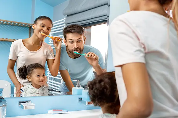 A diverse family brushing their teeth together in the mirror, demonstrating the power of family dentistry. A diverse family brushing their teeth together in the mirror, demonstrating the power of family dentistry.
