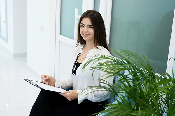 A young woman smiling in the waiting area while filling out paperwork before an appointment.
