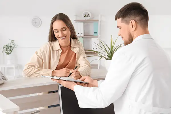 Female patient at a dental office reception desk filling out new patient forms while being assisted by a staff member.